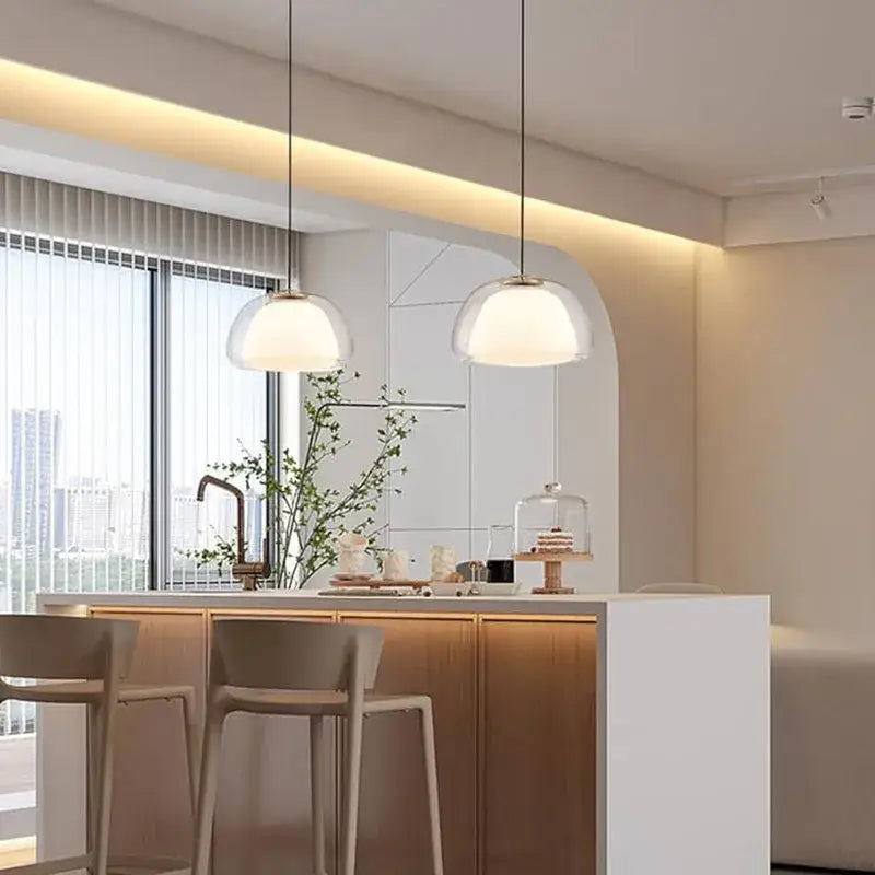 Two modern clear glass jelly pendant lamps with frosted domes and slender metal chains hang above kitchen island