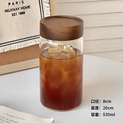 Modern clear glass tea cup with dark brown wooden lid filled with iced coffee for kitchen coffee storage jar