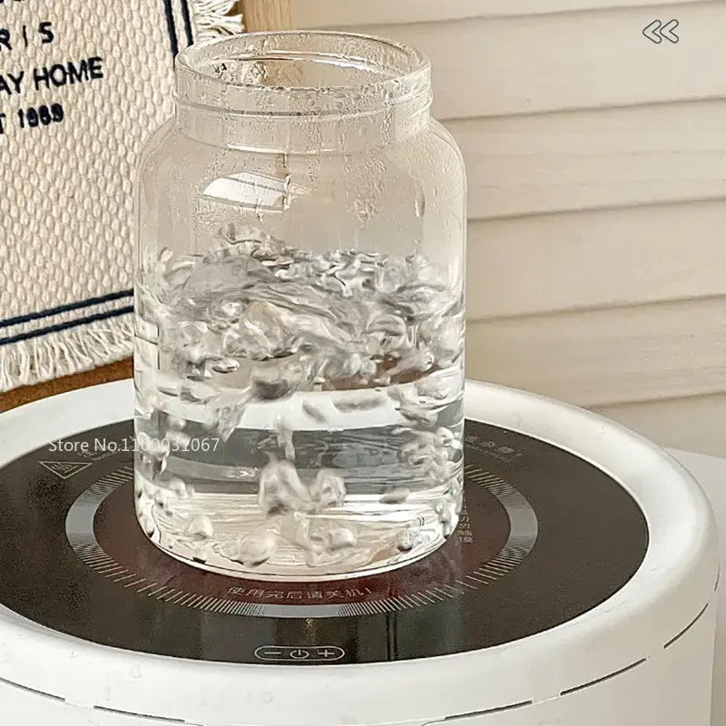 Modern clear glass tea cup with wood lid displaying glass tea jar filled with water on white induction cooktop