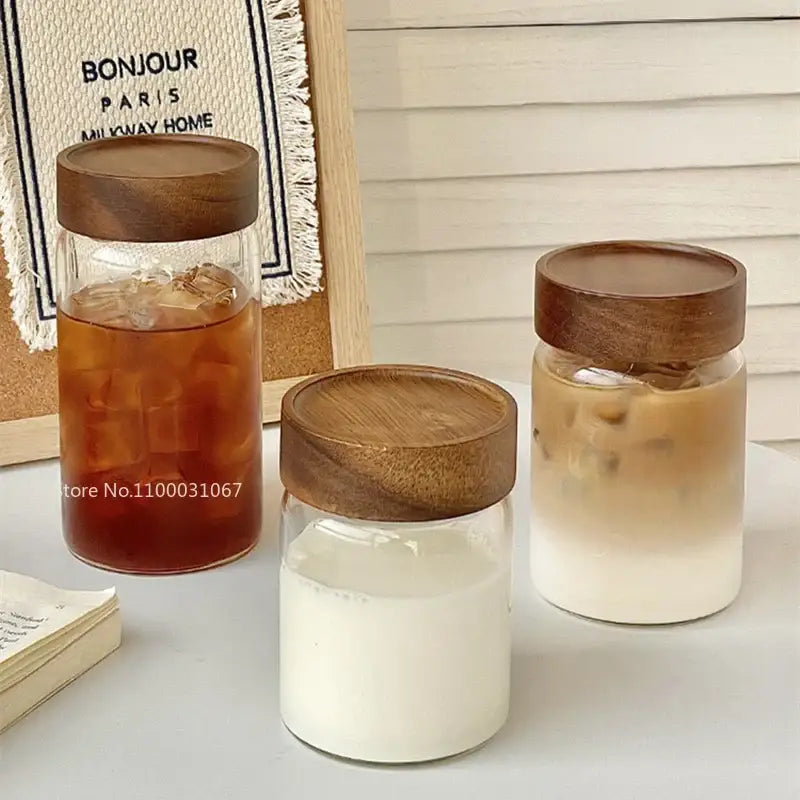 Three clear glass tea cups with wooden lids filled with colored iced beverages for modern kitchen use