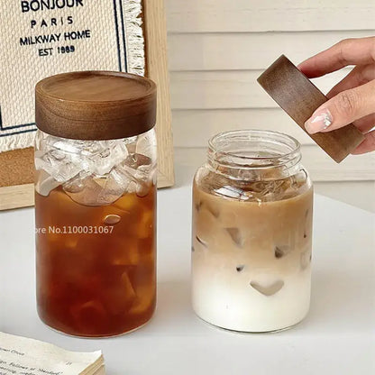 Two clear glass tea cups with wooden lids, one with iced coffee and one with layered iced latte for kitchen use
