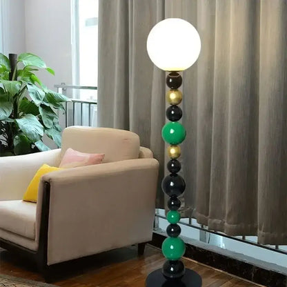 Modern floor lamp with colorful glass ball spheres in black green and gold and a white glass shade for living room use