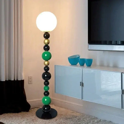 Modern colorful glass ball floor lamp with stacked black green and gold spheres and glowing white bulb for living room use