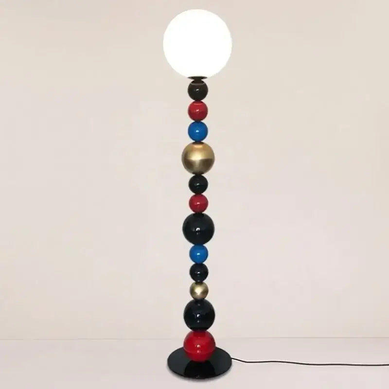 A modern floor lamp with colorful glass ball spheres in red blue black and gold supporting a white globe bulb for living room