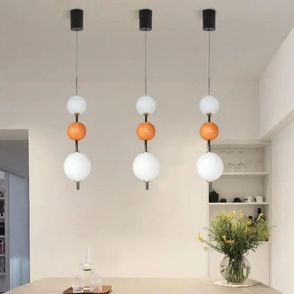 Three modern pendant lights with decorbites glass ball led featuring black mounts and white orange glass orbs for dining room decor