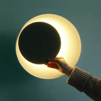 A hand holds a modern colorful rotatable led wall lamp with a frosted white sphere and black inner disc for bedroom use