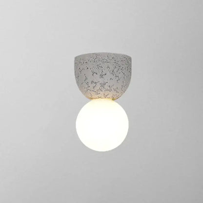 Modern concrete bell wall-mounted light fixture with speckled gray finish and glowing white spherical bulb for bedroom sconce