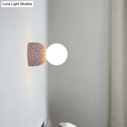 Modern concrete bell wall-mounted light fixture with a speckled pinkish-brown ceramic base and glowing white bulb