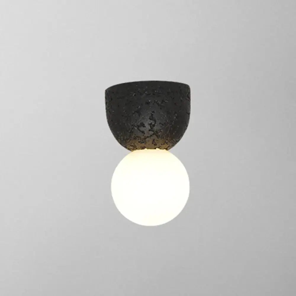 Modern black textured ceramic wall-mounted light fixture with glowing white spherical bulb for bedroom sconce lighting
