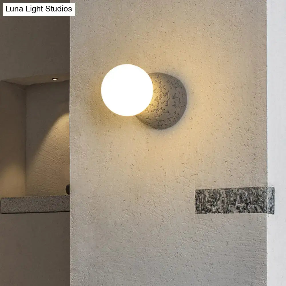 Modern concrete bell wall-mounted light fixture with matte gray textured base and white spherical glass shade for bedroom use
