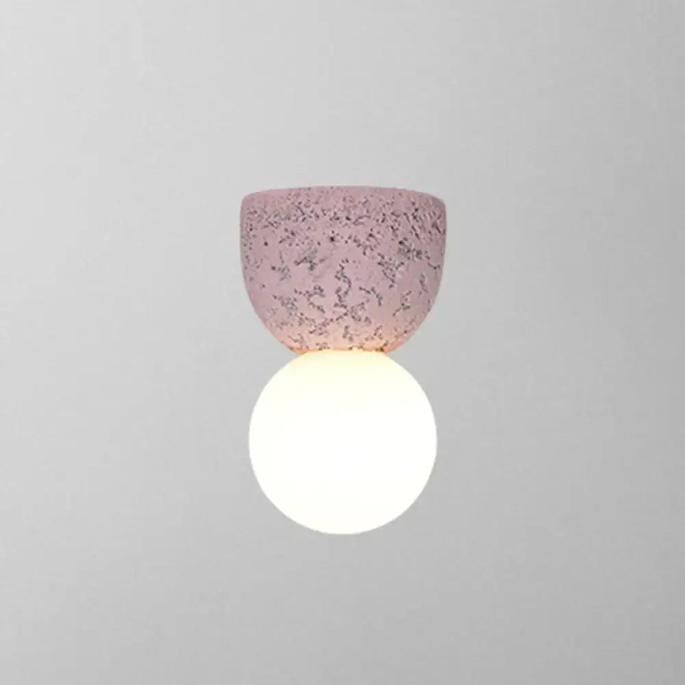 Modern concrete bell wall-mounted light fixture with a soft pink speckled ceramic shade and glowing white spherical bulb