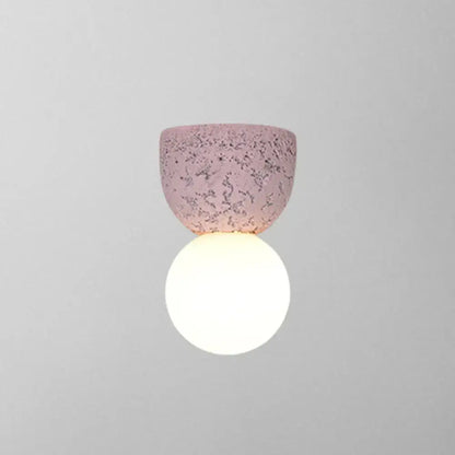 Modern concrete bell wall-mounted light fixture with a soft pink speckled ceramic shade and glowing white spherical bulb