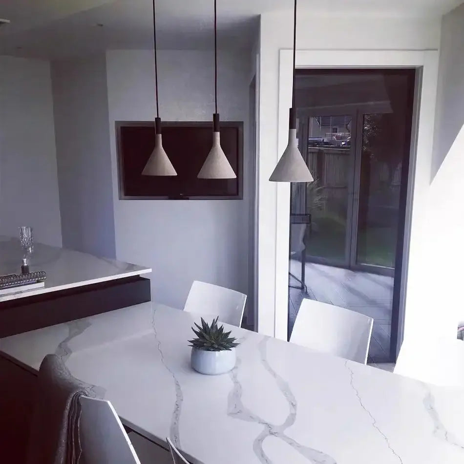 Modern conical concrete pendant lights with sleek black cords hang above a white marble dining table for kitchen decorbites concrete pendant lighting