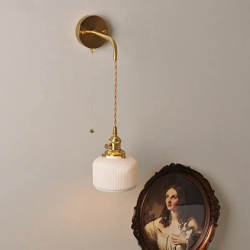 Gold-finished wall light fixture with white ribbed glass shade and twisted cord for modern bedroom lighting