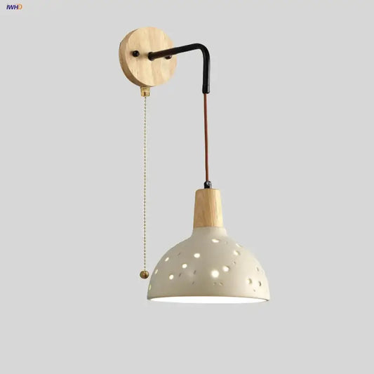 Modern cream ceramic wall lamp with wooden arm and pull chain switch featuring circular cutouts for bedroom lighting