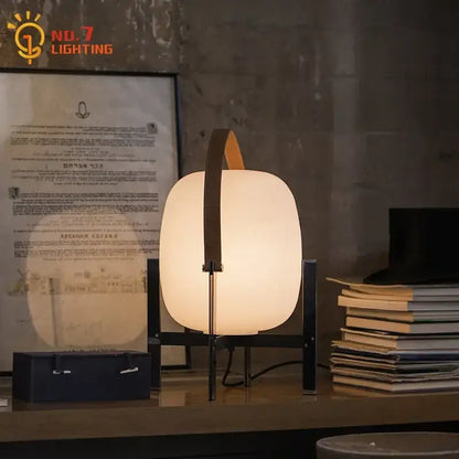 Modern cream designer metal glass table lamp with frosted body, dark frame, and orange leather handle for decorbites decor