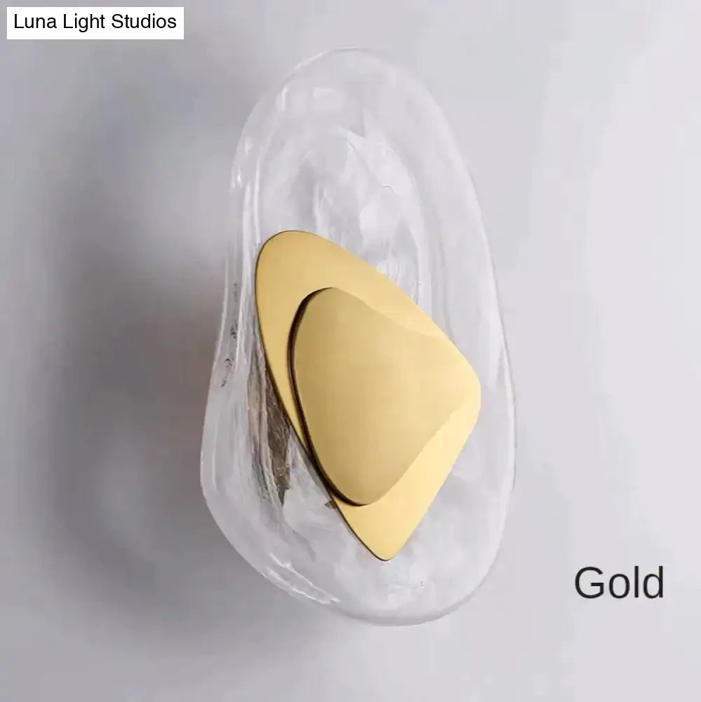 Modern creative minimalist wall sconce with a gold-toned triangular design and transparent glass housing for bedroom lighting