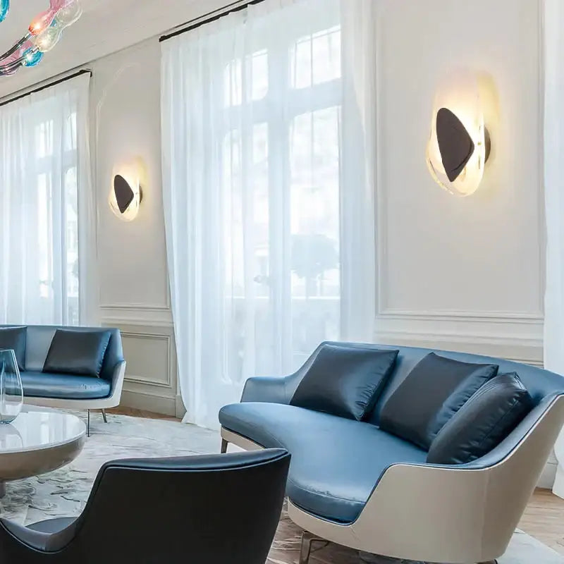 Modern creative minimalist glass wall lamp beside a blue leather sofa with white frame and black cushions for bedroom lighting