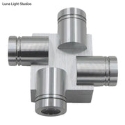 Silver brushed finish cross aluminum wall mount lamp featuring a metallic cross-shaped component with cylindrical ports