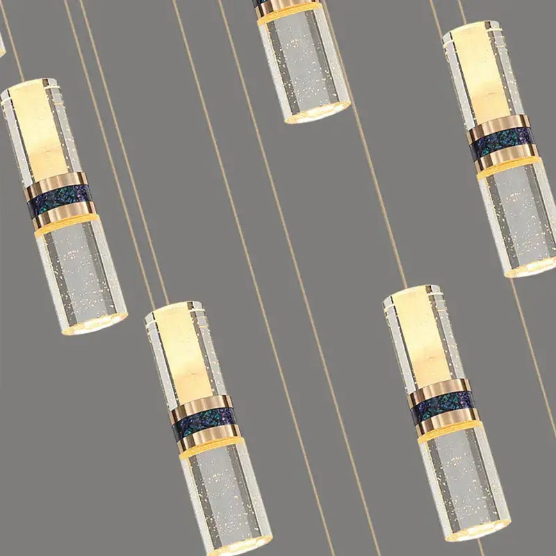 Modern crystal columnar chandelier with cylindrical clear glass and gold-toned bands illuminating a stairwell