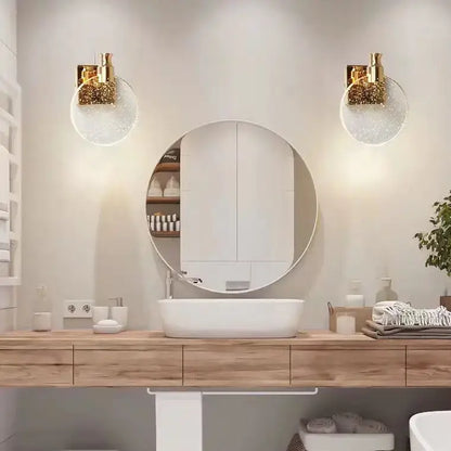 Modern crystal glass gold wall lamp with gold-toned sconces and clear sparkling glass globes flanking mirror above sink