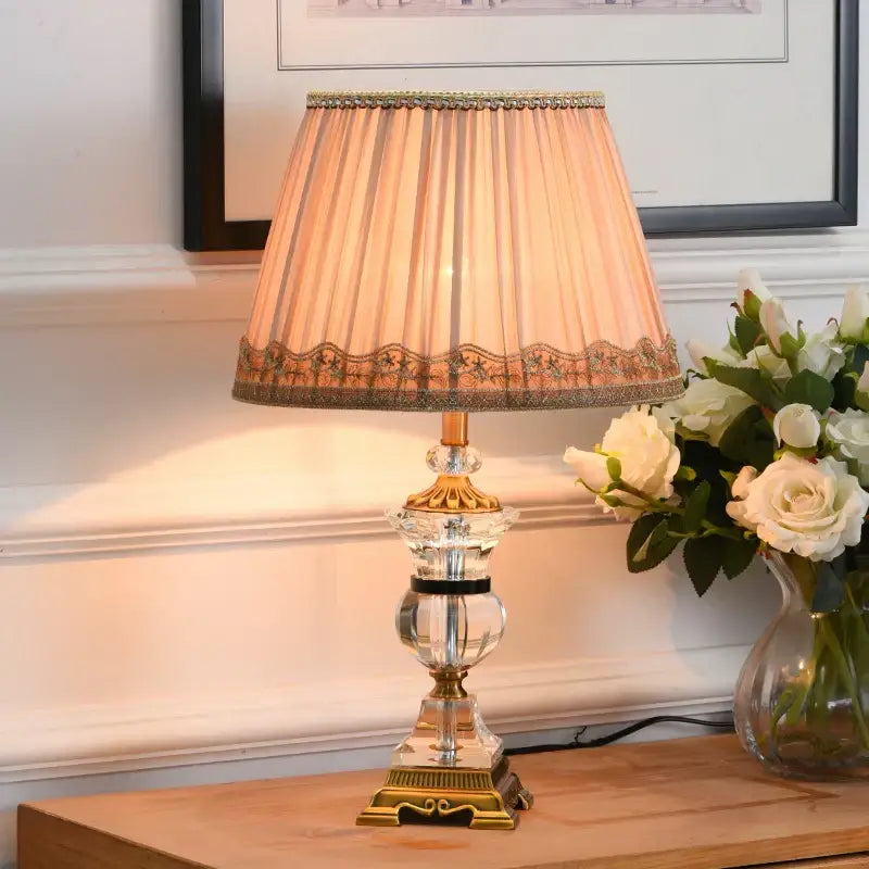 Elegant decorbites crystal table lamp with gold tone base and pleated peach fabric shade featuring cream lace trim