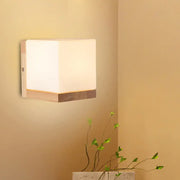 Modern cube shaped sconce wall lamp with frosted white diffuser and wooden backplate for bedroom lighting