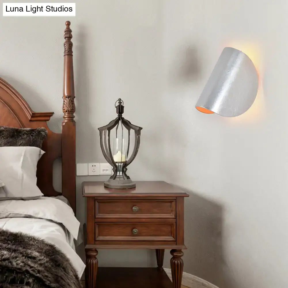 Modern curved silver cylindrical wall sconce light with warm interior glow for bedroom ambient lighting in black grey tones