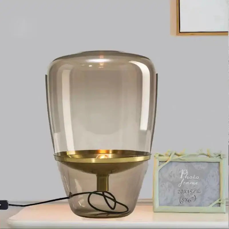 A modern decorbites glass table lamp with a translucent amber glass shade and polished brass base for bedroom lighting