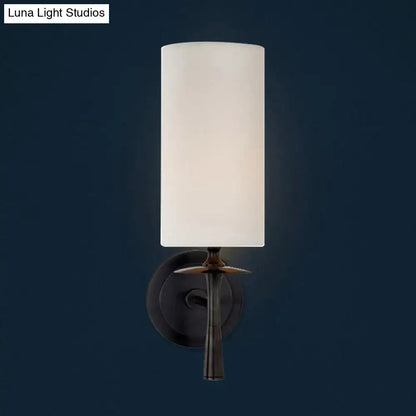 Modern dark bronze sconce light with a sleek cylindrical white glass shade and elegant leaf-like metal design for bedroom use
