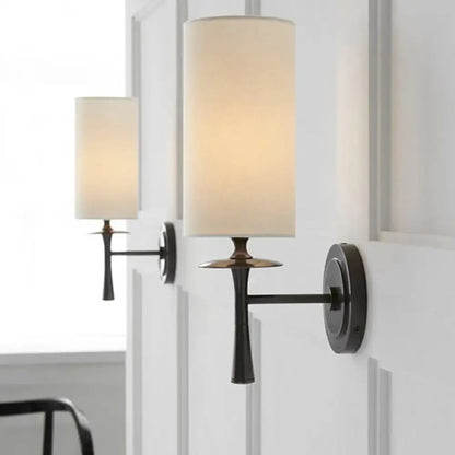 Modern dark bronze sconce light with warm-toned cylindrical fabric shade and white glass shade bedroom fixture