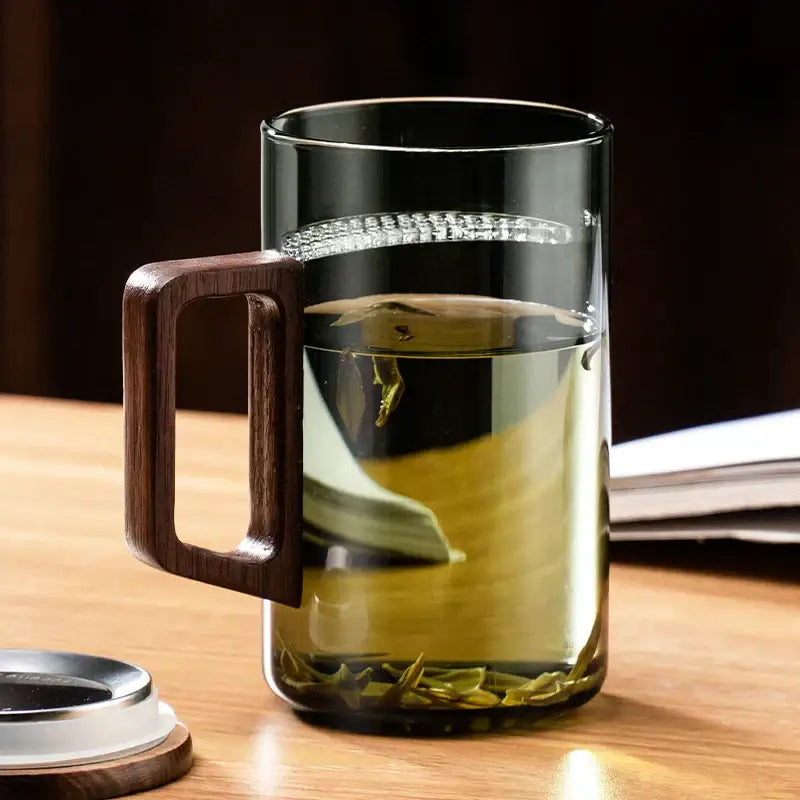 Modern dark green glass tea cup set with clear glass mug, dark wood handle, and silver lid beside it for dining room use