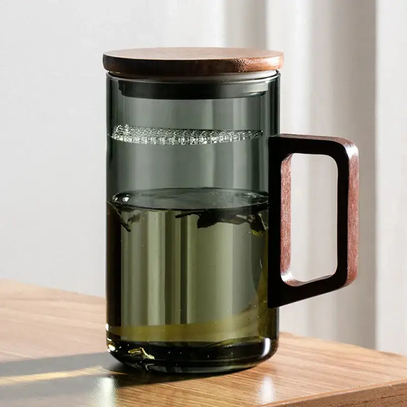 Modern dark green glass teapot with wooden lid and handle as part of a sleek tea cup set for dining room use