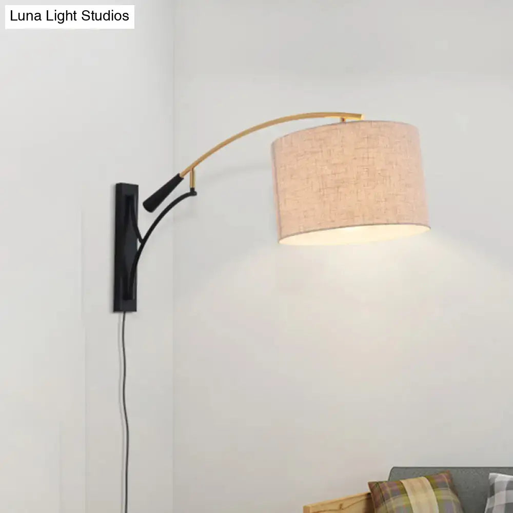 Beige linen textured modern drum shade wall lamp in flaxen coffee mounted on a curved brass arm with black bracket