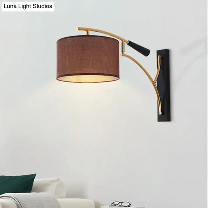 Modern drum shade wall lamp in flaxen coffee with a warm brown fabric shade and gold metal arms for bedroom use