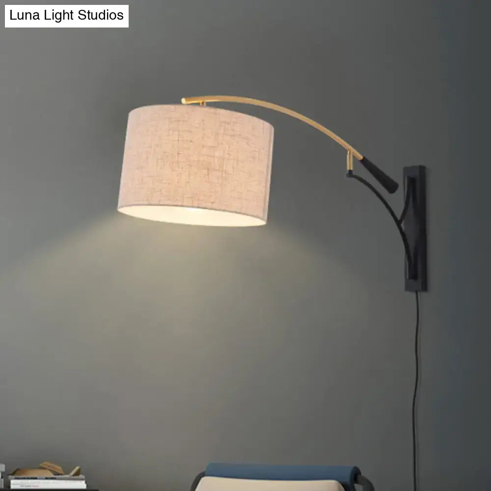 A modern drum shade wall lamp with flaxen coffee beige linen shade and brass-finished arm for bedroom use