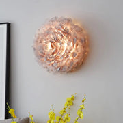 A modern wall light featuring feather material in grey and white tones designed for bedroom use