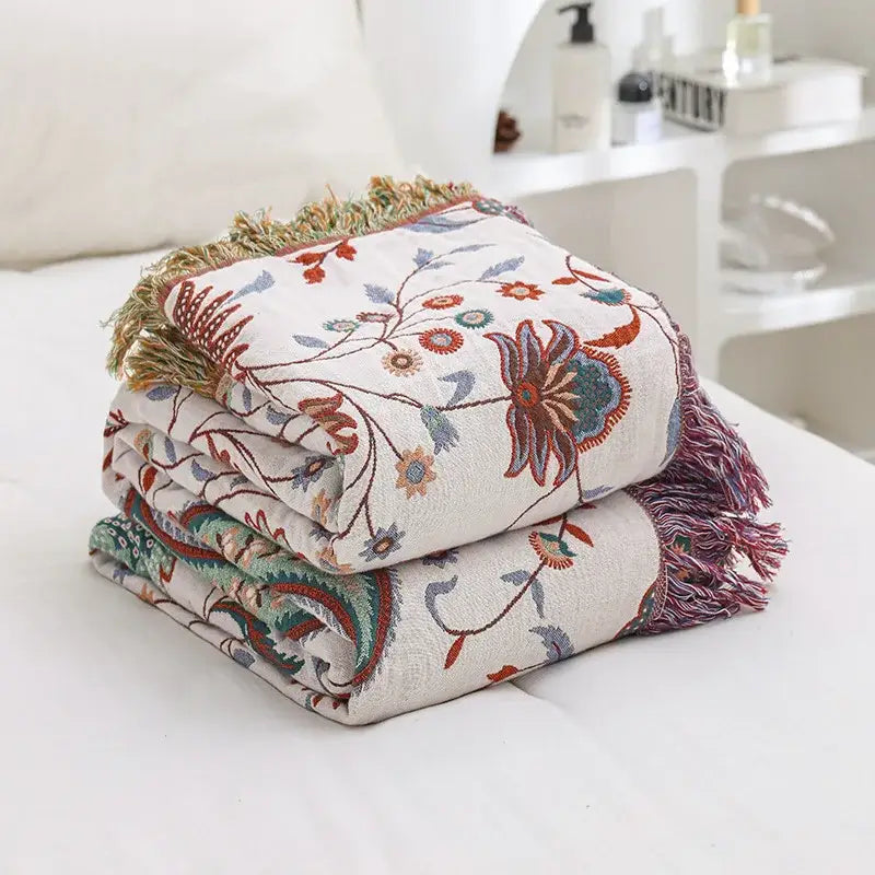 A folded cream cooling cotton blanket with rust teal floral embroidery and fringed edges by decorbites cooling cotton