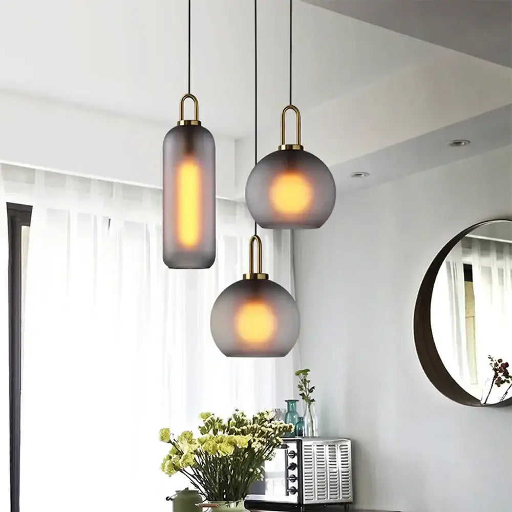 Three modern frosted gray glass ball pendant lights with brass accents hang from black cords in a dining room decorbites glass ball pendant set