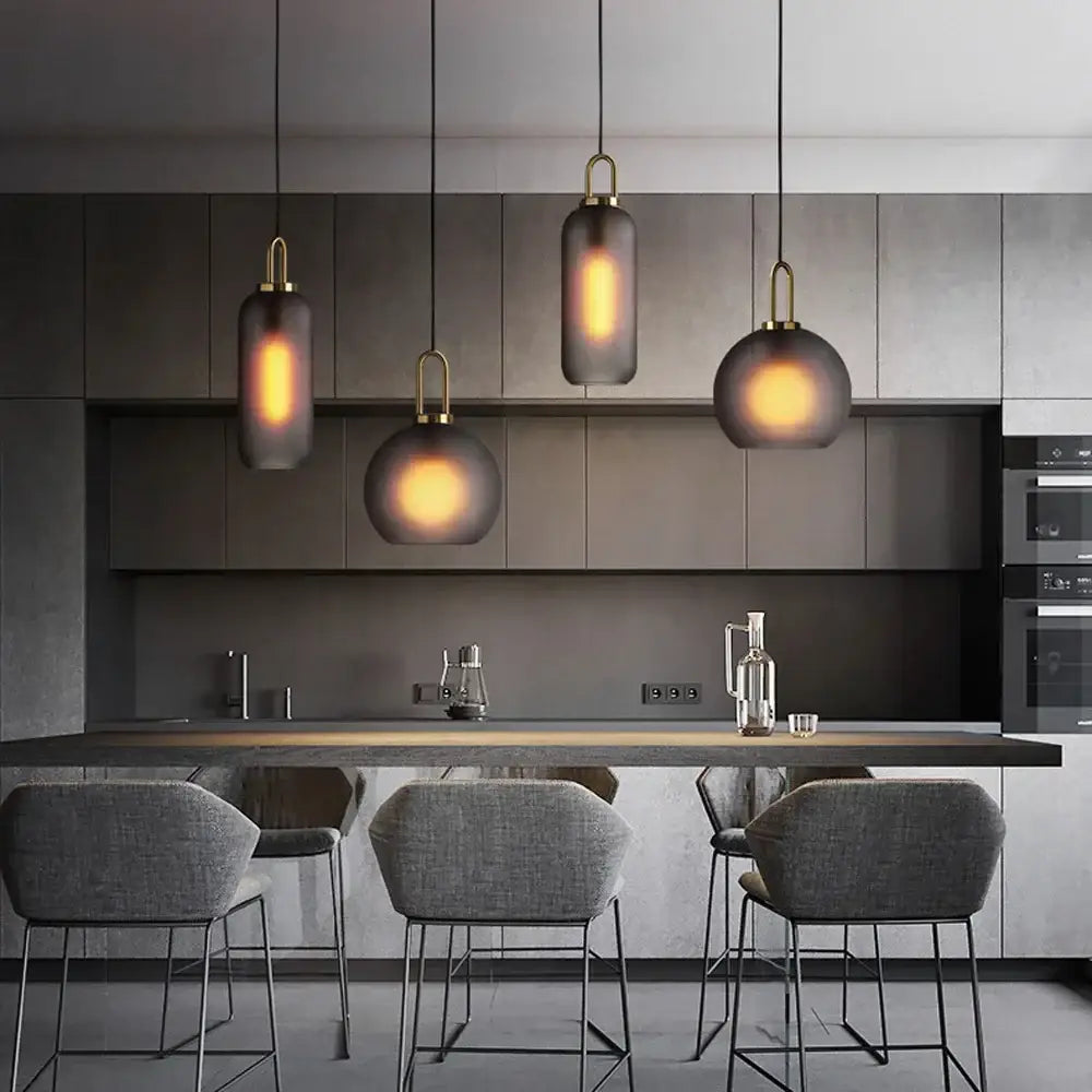 Three modern brass accented pendant lights with smoked glass shades hang above a dark kitchen island decorbites glass ball