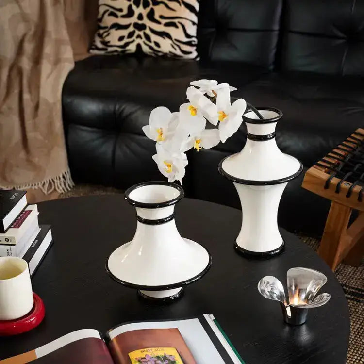 White ceramic vases with black rims and flared bases hold white orchids in modern geometric black and white stripes decorbites vase