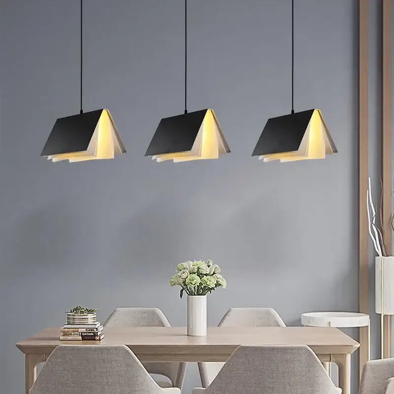 Three black book pendant lamp lights with warm yellow interiors hang above a dining table for modern bedroom decorbites
