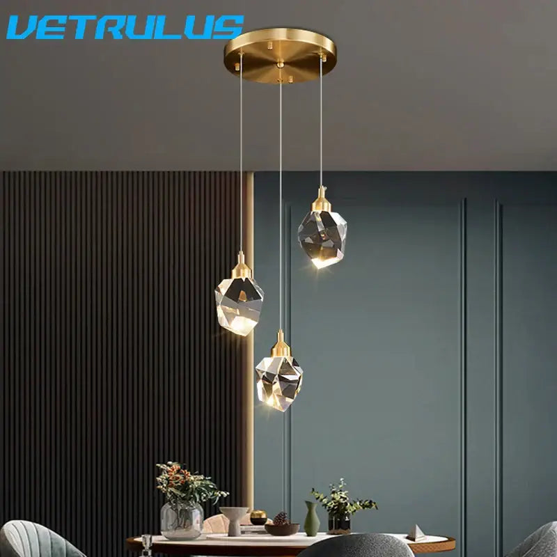 Gold-toned modern geometric pendant light with faceted diamond crystal led shades in a circular crystal led chandelier design