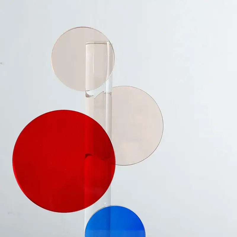 A modern geometric crystal circle sculpture with red blue and beige discs on clear rods for home decor