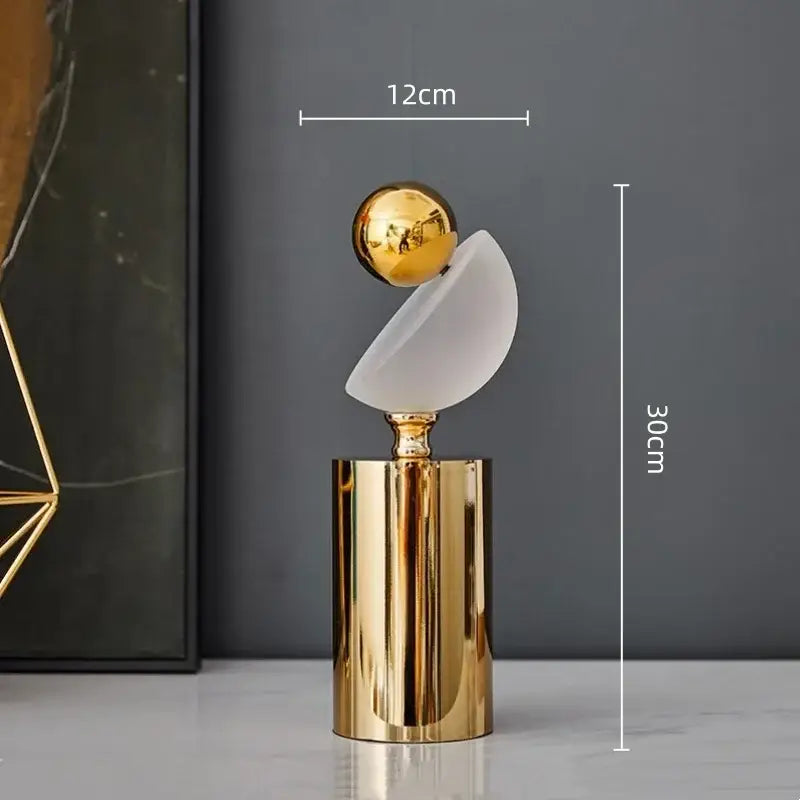 A modern geometric golden ball sculpture with a frosted glass disc on a gold-toned cylindrical base for living room decor