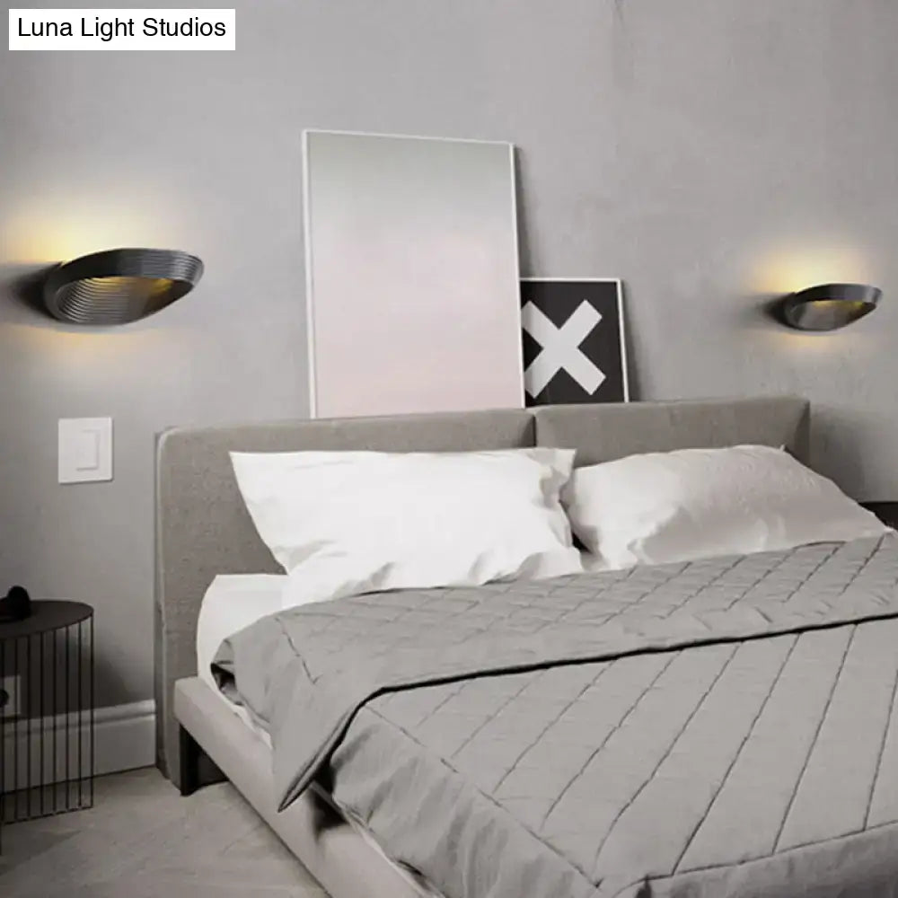 Modern geometric black metal wall light with sleek curved design providing warm white light for bedroom ambiance