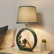 Modern girl reading teal resin night lamp with a golden figurine and a textured beige fabric shade for bedroom use