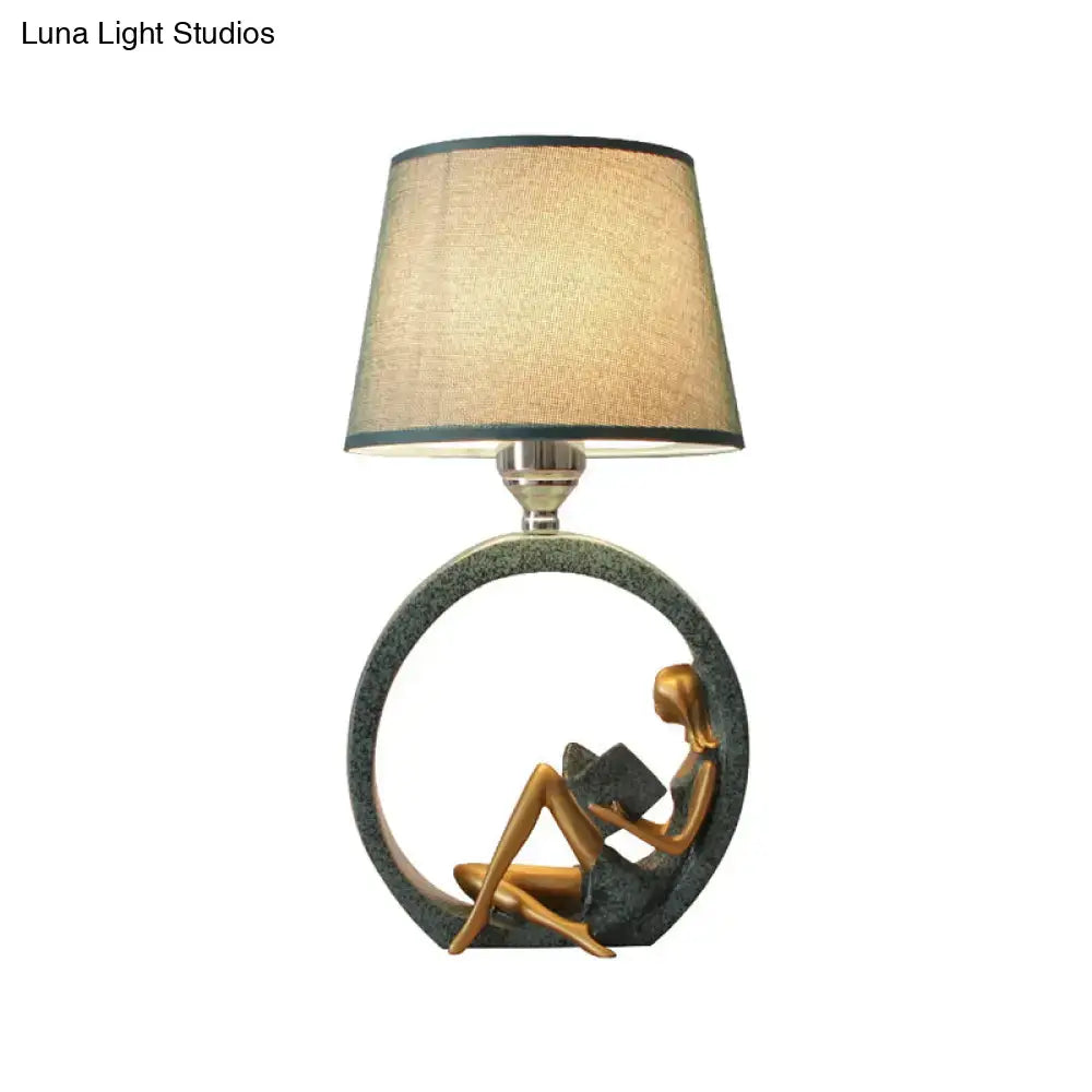 Bronze-colored resin night lamp of a modern girl reading with a fabric shade on a circular base for bedroom use