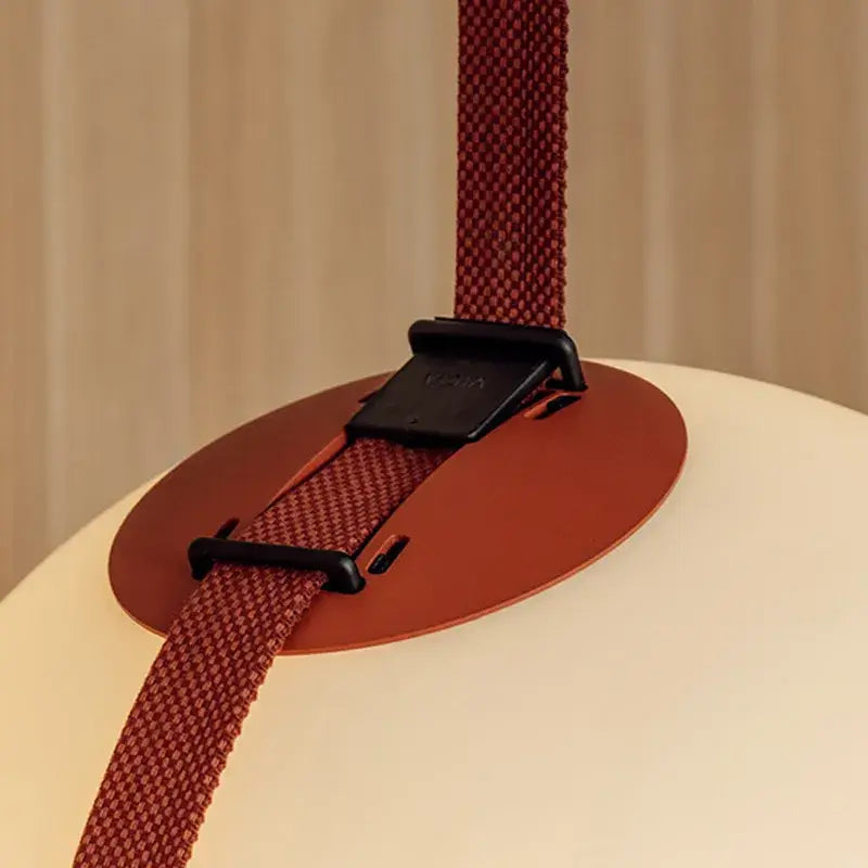 Red woven strap with black buckle securing orange base on off-white lampshade of decorbites glass ball led pendant light
