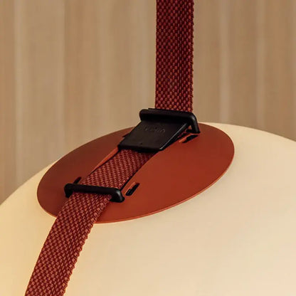 Red woven strap with black buckle securing orange base on off-white lampshade of decorbites glass ball led pendant light